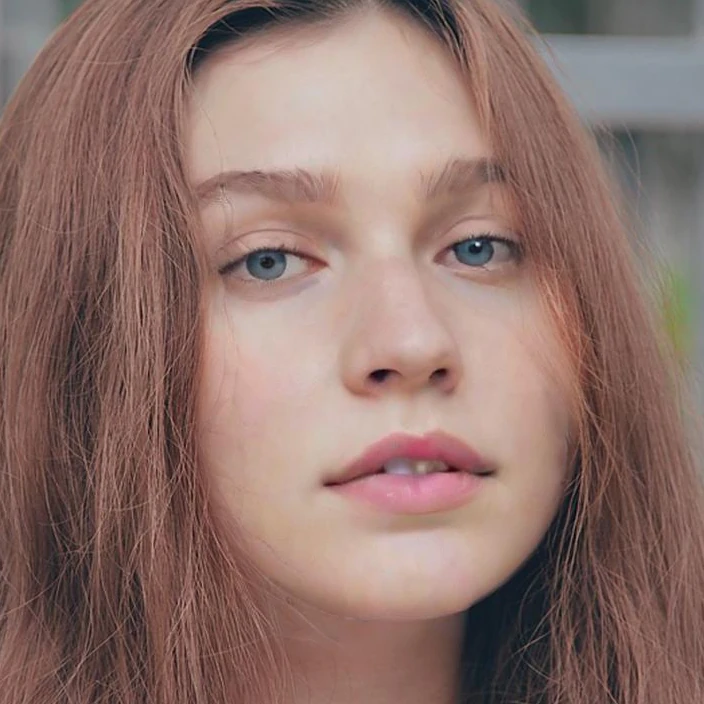 Close-up of a woman with long auburn hair looking at the camera with her lips slightly parted, before the v2 update